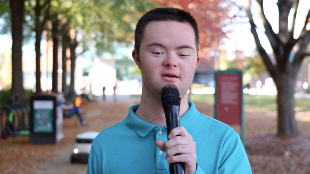 A disabled student talks into a handheld microphone towards the camera.