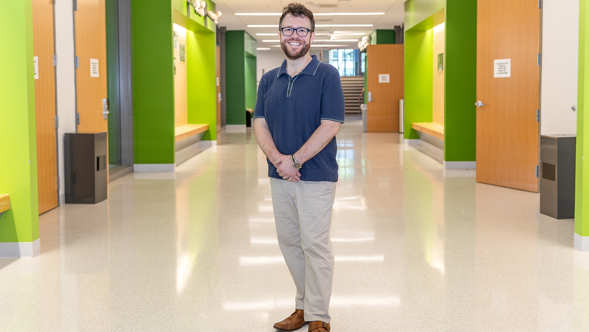 A man stands with a smile in an academic hallway.