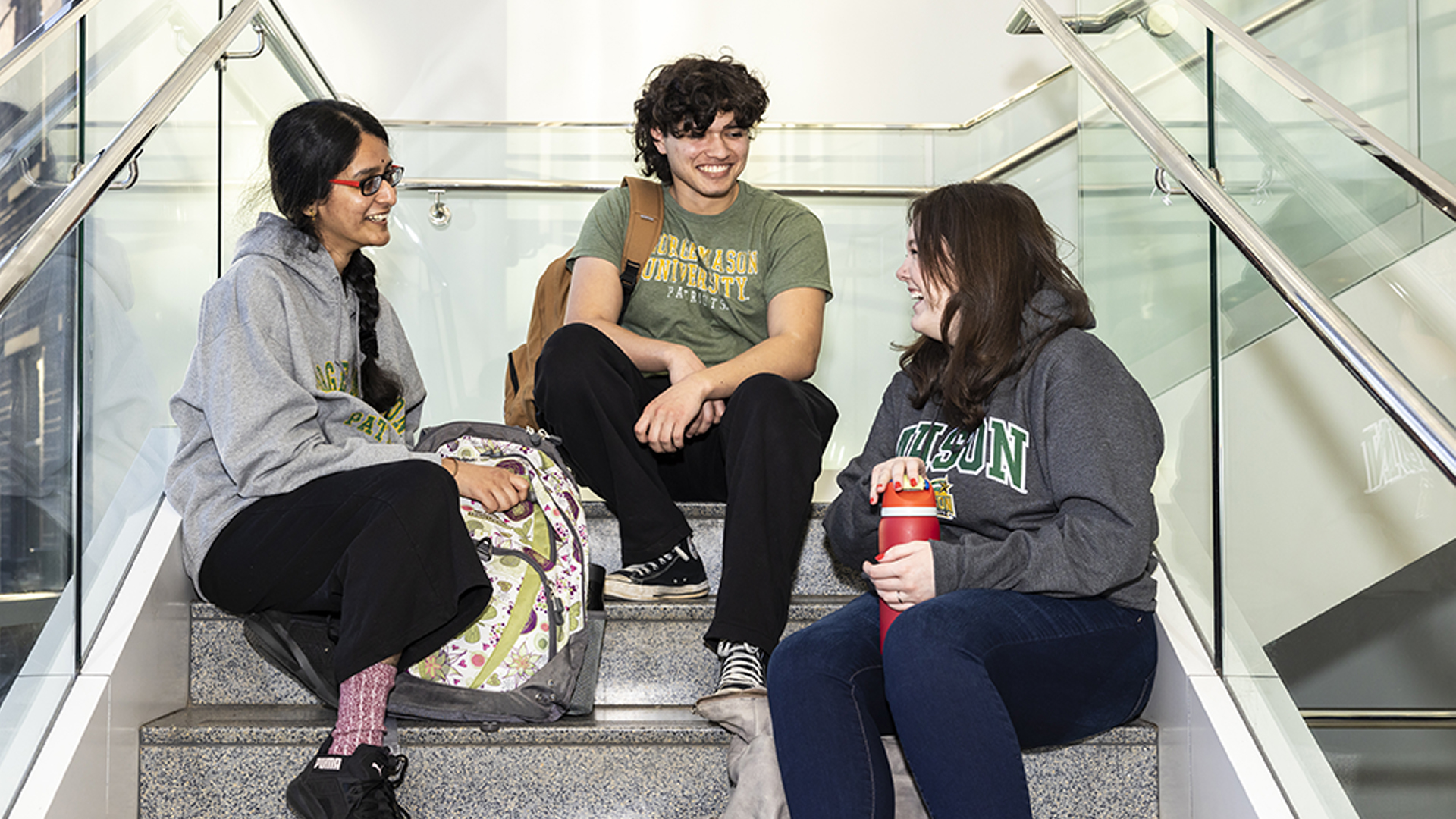 A group of three George Mason University students sitting on the stairs and happily chatting.