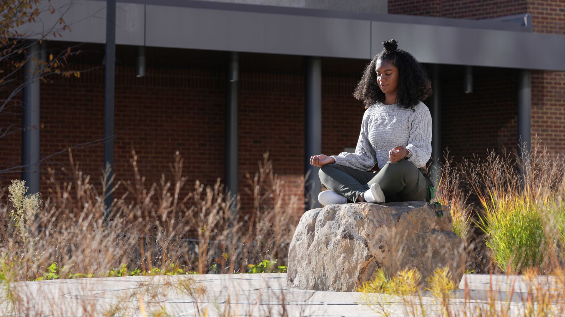 A student meditates on a boulder on campus.